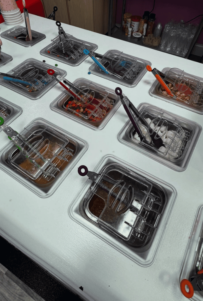 An overhead view of a white table displaying various black plastic storage containers filled with organized hardware, tools, and fasteners.