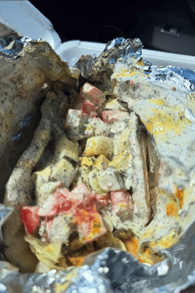 A close-up overhead view of a loaded sandwich with meat, cheese, and vegetables served on a white plate in what appears to be an outdoor setting.