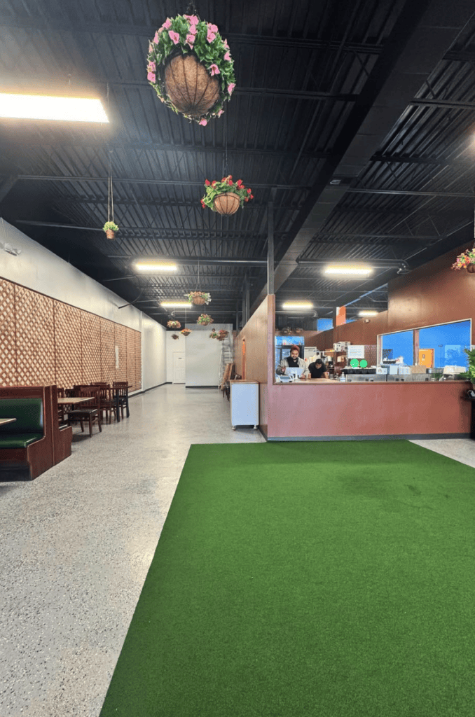 A modern indoor golf simulator facility with artificial turf, reception desk, and contemporary lighting fixtures in a clean, well-designed space.