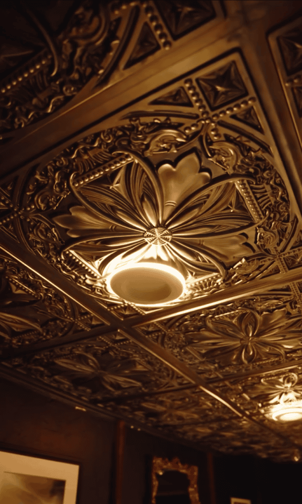 An ornate, intricately carved ceiling fixture with warm golden lighting showcasing classical architectural detailing and decorative plasterwork in an interior venue.