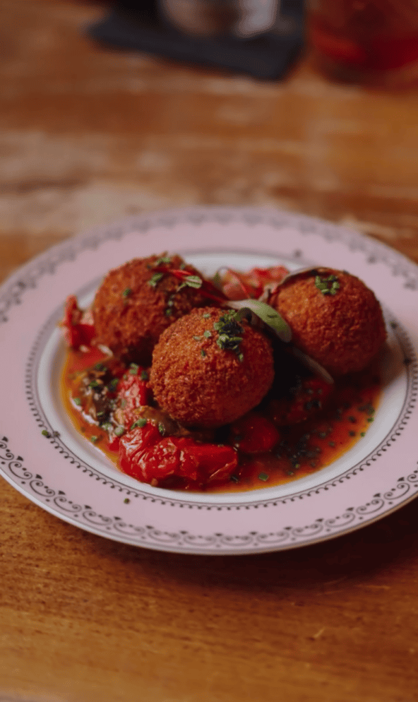 A plate of Italian meatballs in rich red tomato sauce served on a decorative white plate on a wooden table.
