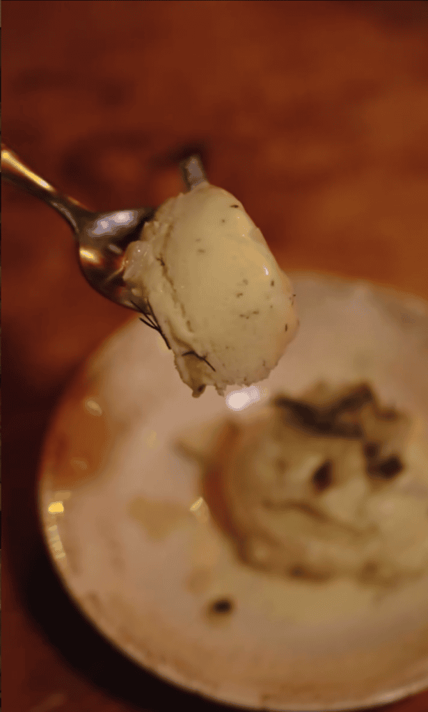 A close-up shot of a spoon lifting a creamy dessert or sauce from a plate, captured in warm, soft lighting.