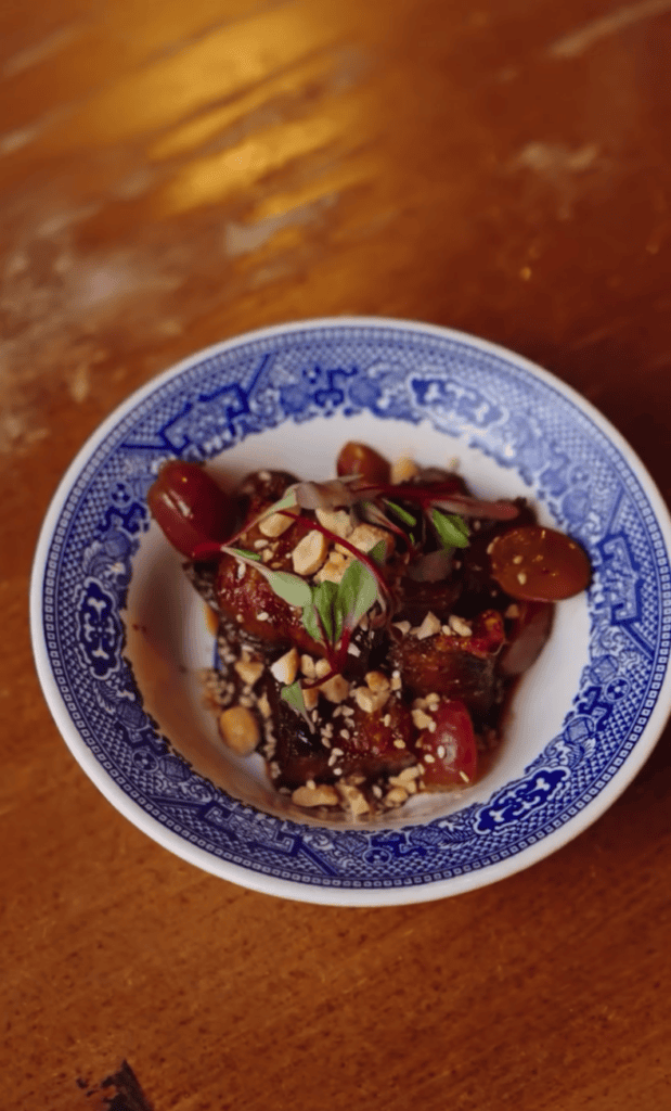 An overhead view of an Asian noodle soup dish served in a decorative blue and white bowl on a warm wooden table surface.