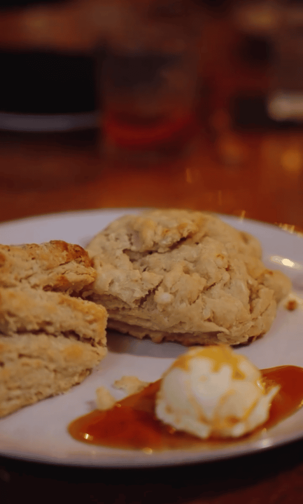 A close-up plate of freshly baked scones with whipped cream and sauce garnish in a warm, indoor dining setting.