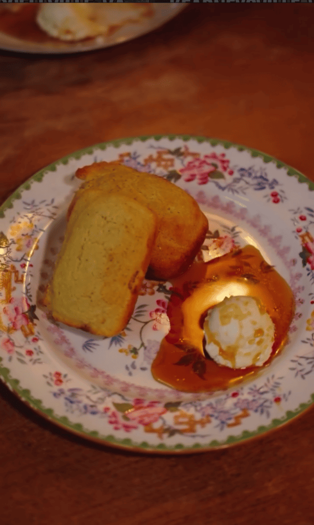 A plated dessert featuring golden cake, pastries, and sauce arranged on a decorative floral-patterned plate against a warm terracotta background.