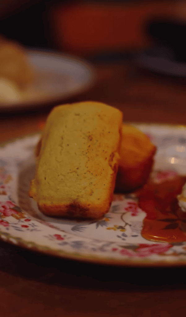 A close-up of golden-brown baked pastries plated on a decorative dish with red sauce drizzle in an indoor dining setting.
