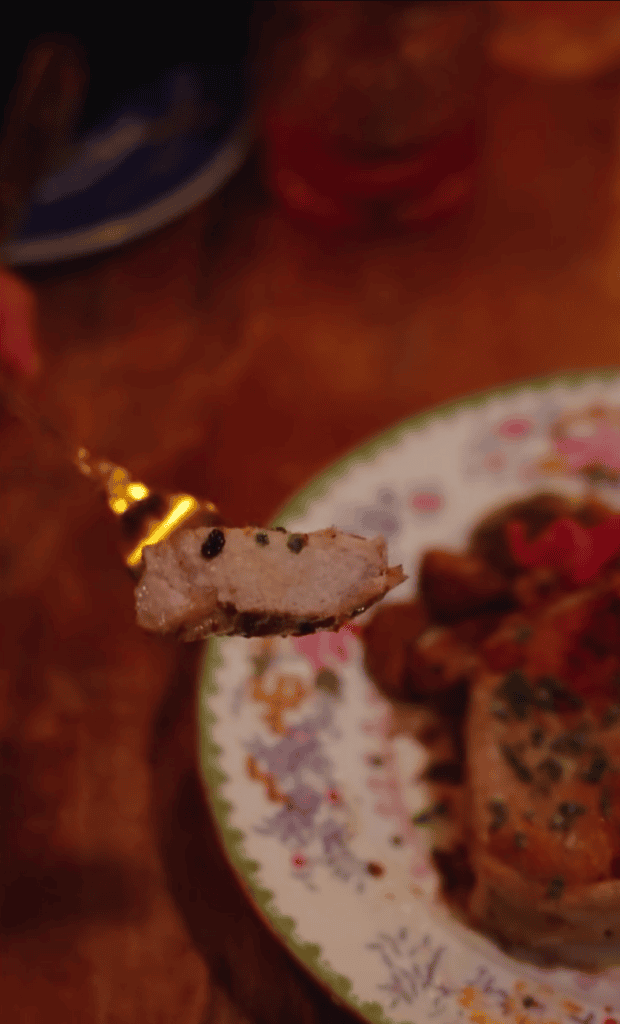 A close-up of a lizard perched on a decorative plate with food and drinks visible in a warm-toned indoor setting.