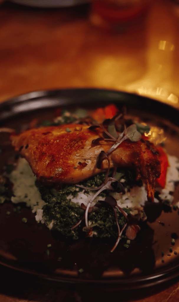 A freshly cooked lobster is plated on a black dish with garnish, photographed in warm indoor lighting.