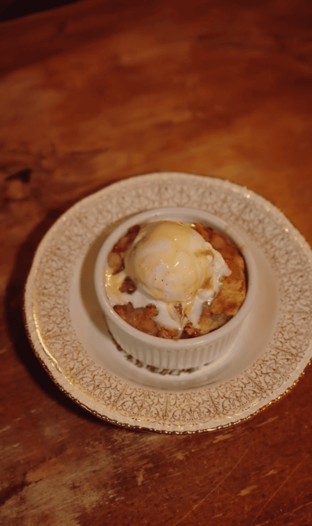A single baked appetizer or tartlet topped with melted cheese and garnish sits on a decorative plate against a warm wooden surface.