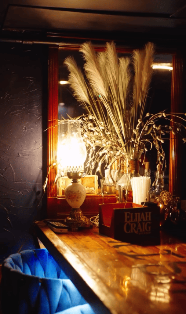 An elegant indoor venue setup featuring a golden dried grass floral arrangement with candles creating dramatic warm lighting on a wooden surface.