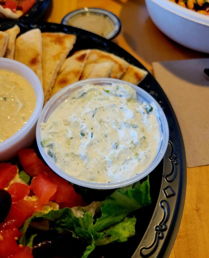 An overhead view of an appetizer platter featuring creamy dips, fresh vegetables, and tortilla chips arranged on decorative ceramic bowls.