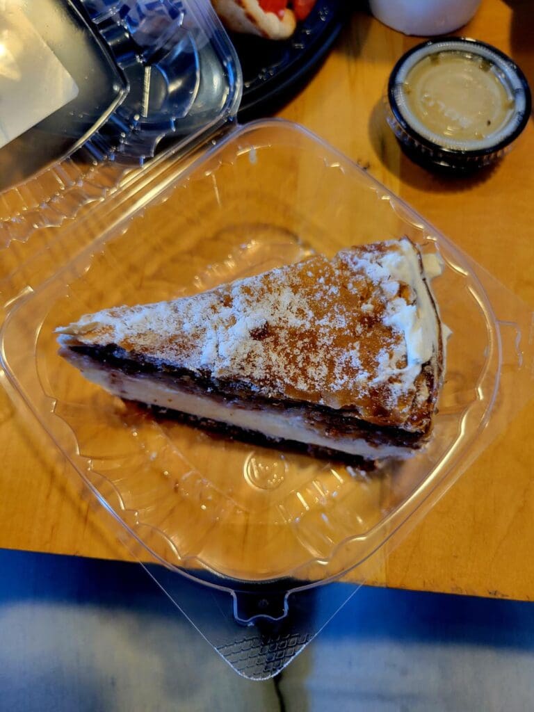 A powdered sugar-coated pastry with dark chocolate filling sits on a clear plastic plate in an indoor food setting.
