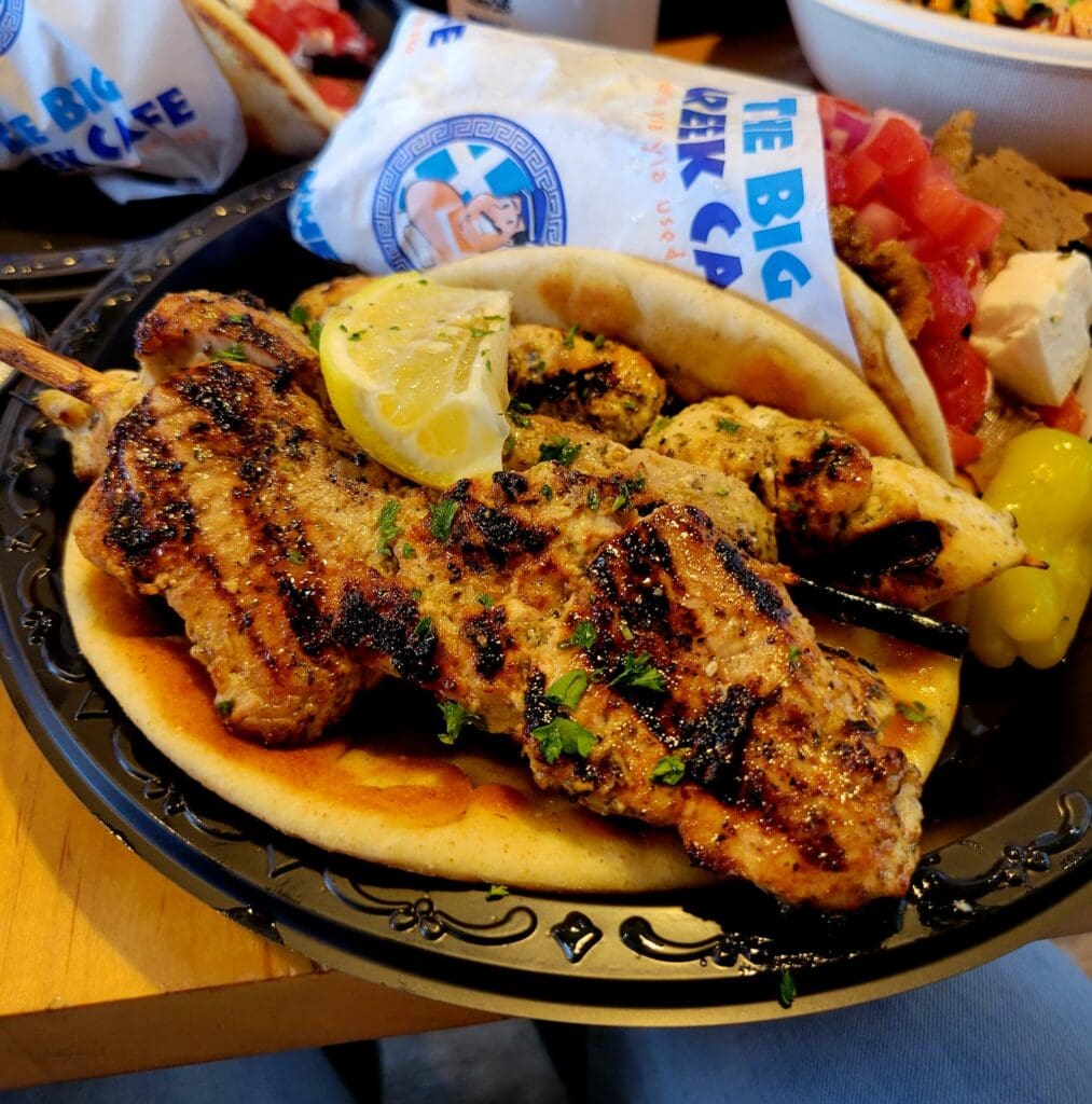 A close-up of charred grilled meat skewers served on flatbread with vegetables and sauce on a decorative ceramic plate.