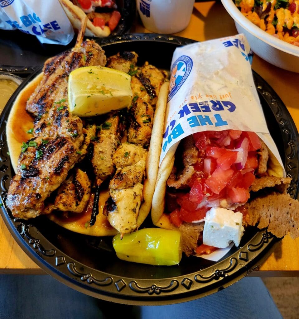 An overhead view of a decorative platter featuring grilled meats, tortillas, fresh tomatoes, and lime served at what appears to be a Mexican restaurant or food establishment.