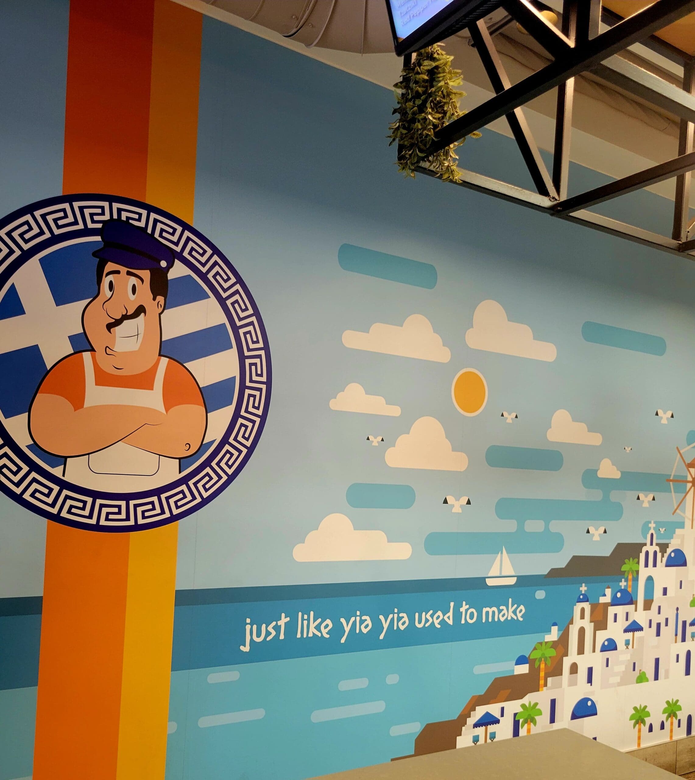 A themed indoor venue features a large Hercules-inspired mural with Mediterranean architectural elements, clouds, and motivational text against a blue sky background.
