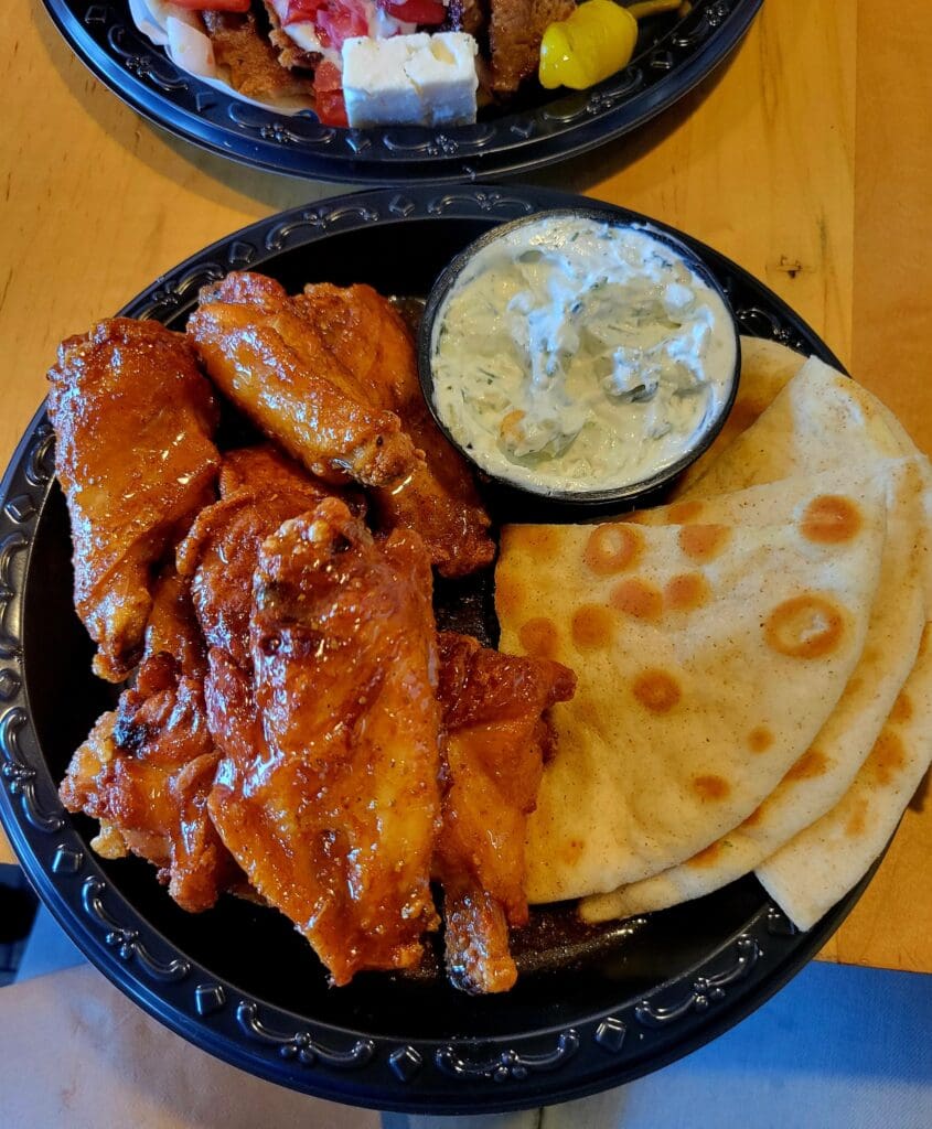 An overhead view of two plates with cooked breakfast items including bacon, flatbread, and fresh cucumber slices on wooden surface.