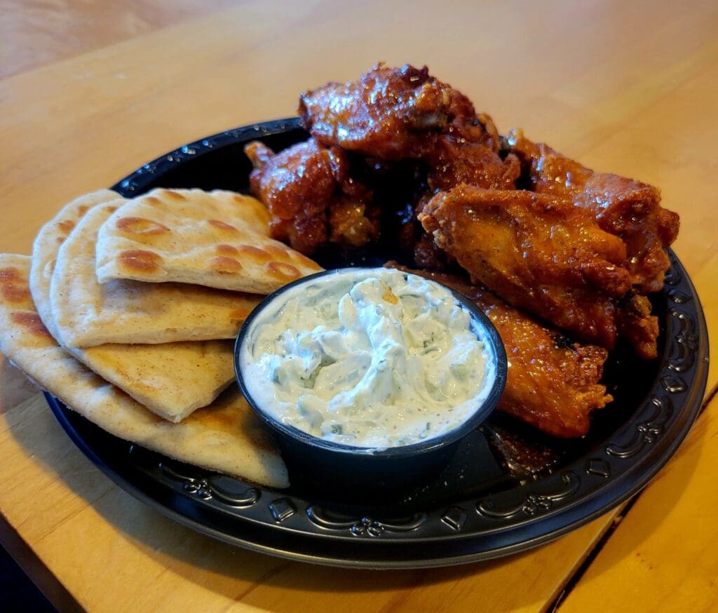 A platter of golden fried chicken served with warm pita bread and a white dipping sauce on a black plate.