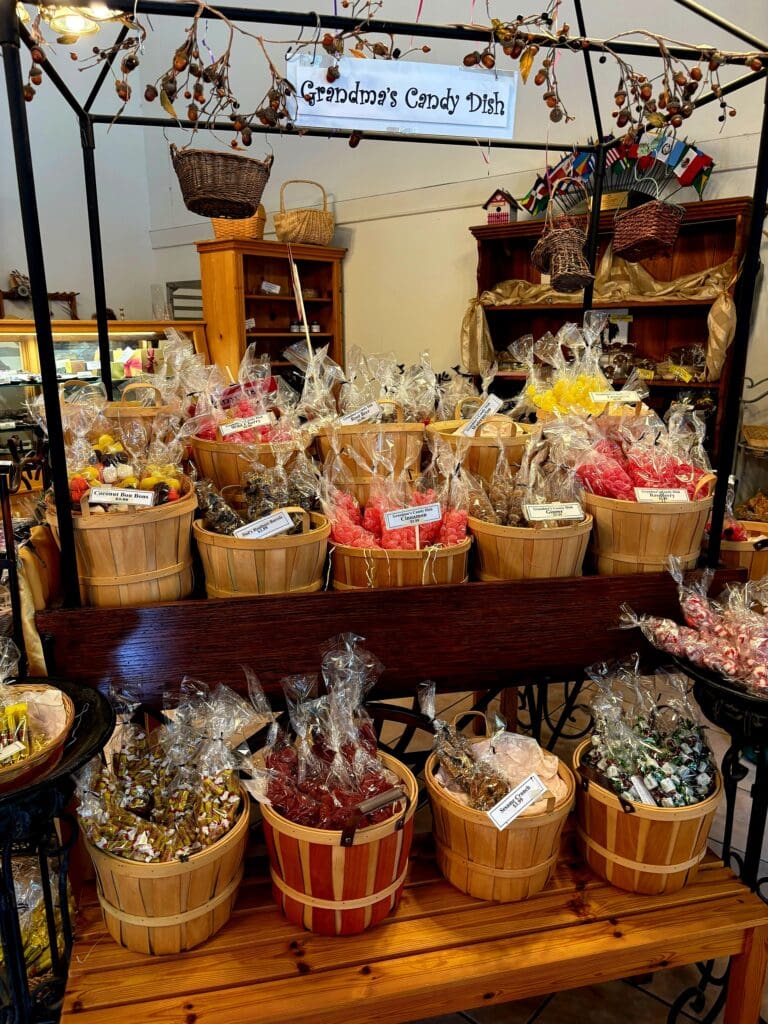 A carnival or fair candy stand displays colorful popcorn and sweets in wooden baskets and containers with a vendor signage visible overhead.
