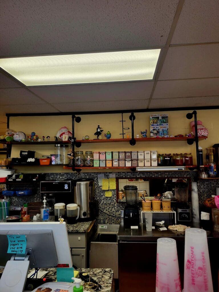 A well-organized workshop or craft room features a dark counter with shelving above, fluorescent ceiling panels, and various storage containers and supplies arranged throughout the space.