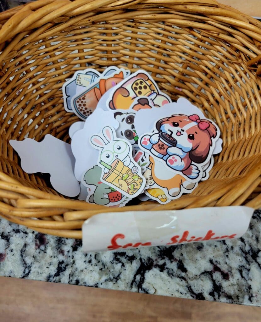 Colorful decorative stickers featuring cartoon characters are displayed in a woven basket on a marble surface, suggesting a craft or hobby workspace.