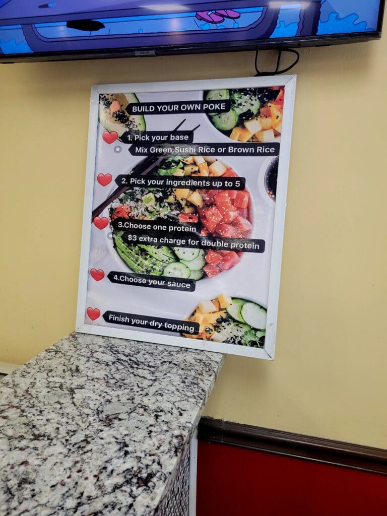A laminated food menu board displaying various dishes is mounted on a yellow kitchen wall above a granite countertop, with a television visible above.