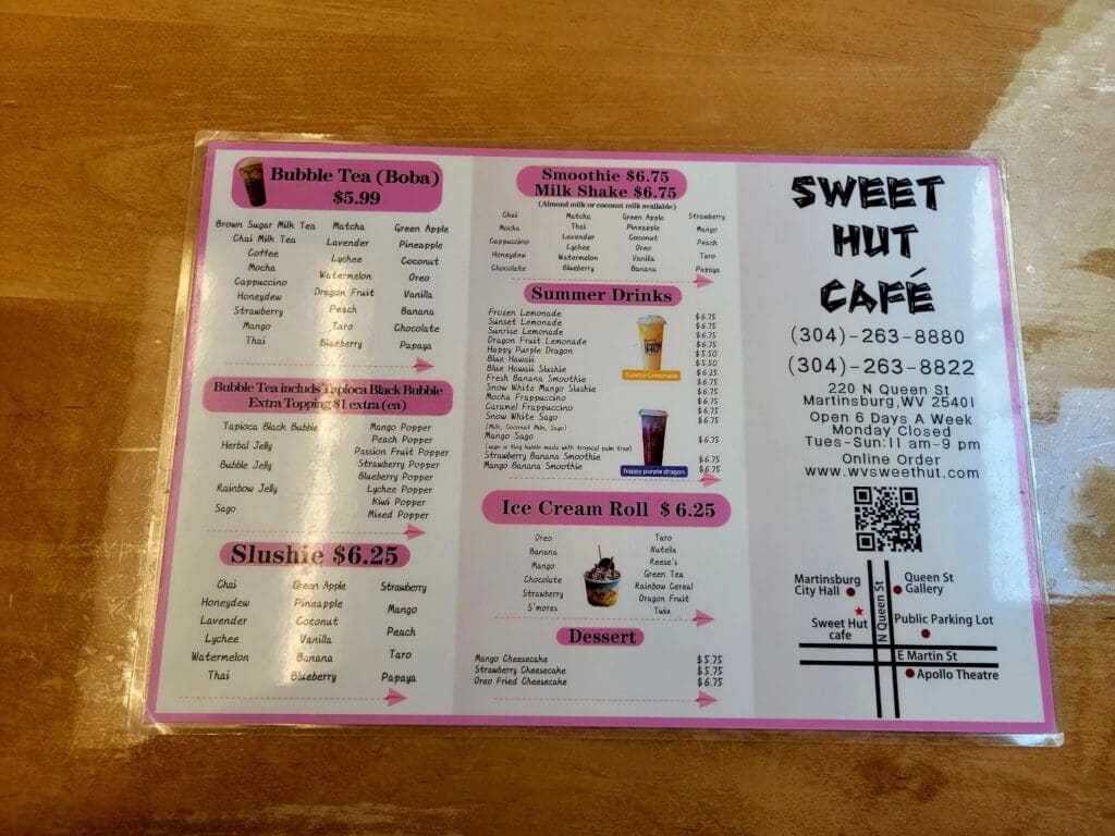 A laminated menu board from Sweet Hut Cafe displaying beverages, prices, and location information with a QR code.