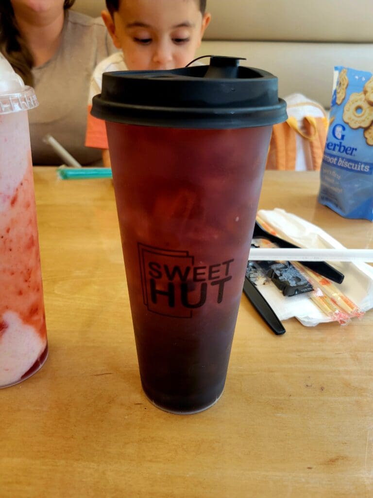 A dark red reusable beverage cup sits on a wooden table during an indoor workshop or activity with children present.