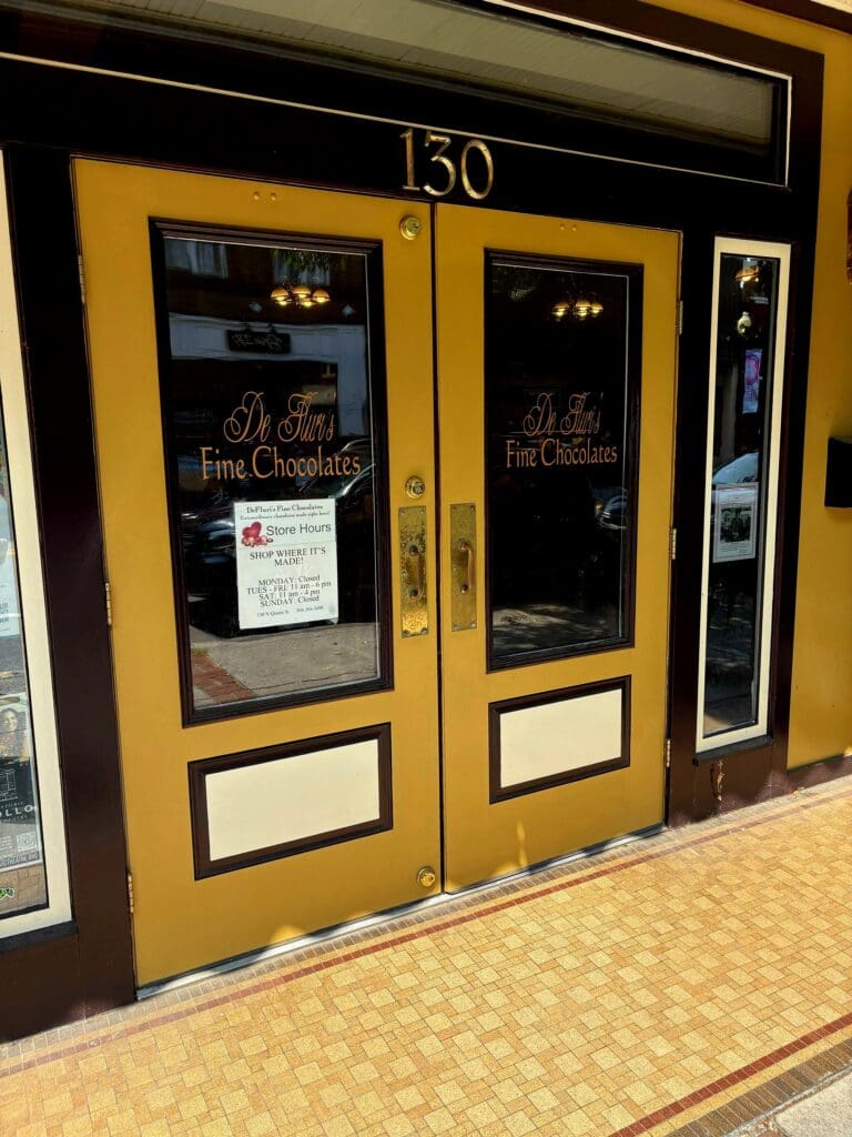 A storefront entrance numbered 150 featuring bright yellow double doors with dark trim and tiled flooring in an indoor shopping or commercial venue.