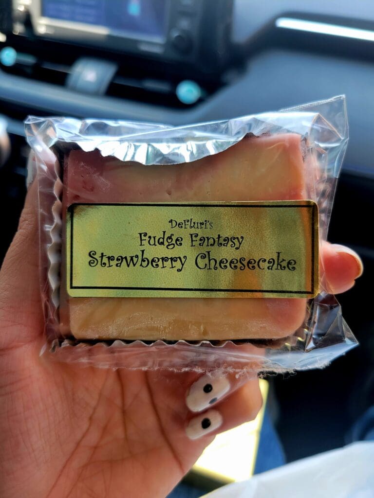 A hand holds a packaged strawberry cheesecake dessert with a yellow-green product label visible in daylight.