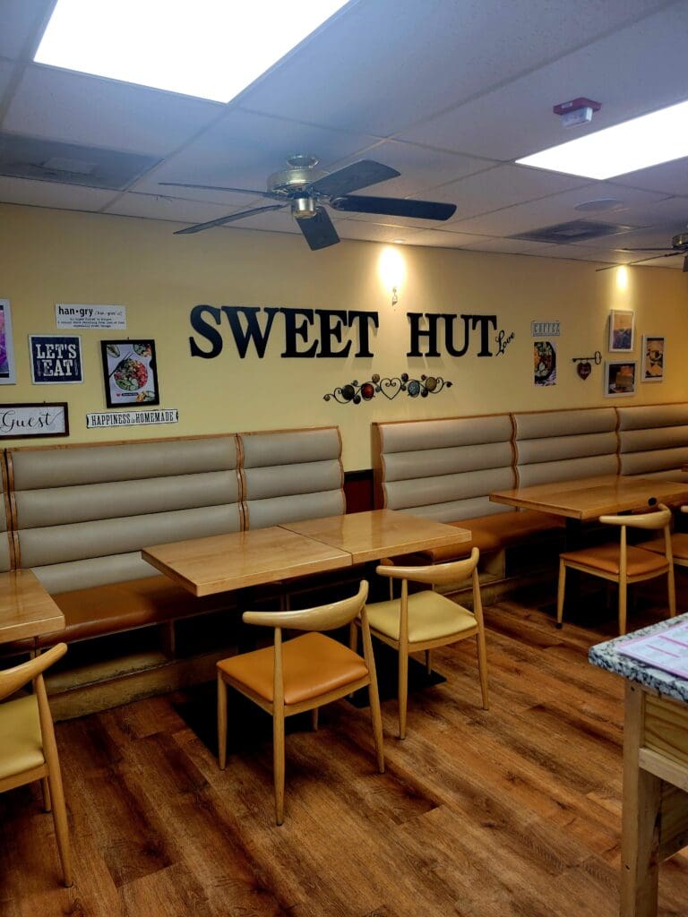 An empty casual dining restaurant interior with booth seating, wooden tables, and a prominent 'Sweet Hut' sign on the yellow wall.