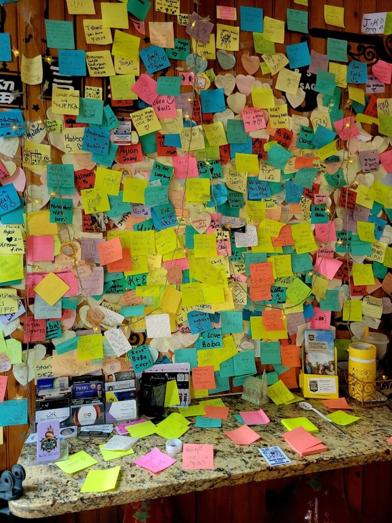 A heavily decorated wall and desk covered with colorful sticky notes and papers creating a vibrant, chaotic workspace.