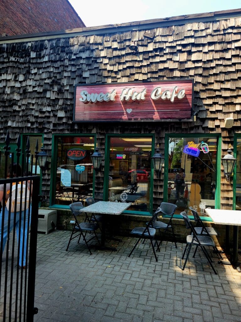A casual outdoor food vendor storefront with brick walls, neon signage, and outdoor seating areas in what appears to be an urban courtyard or alley setting.