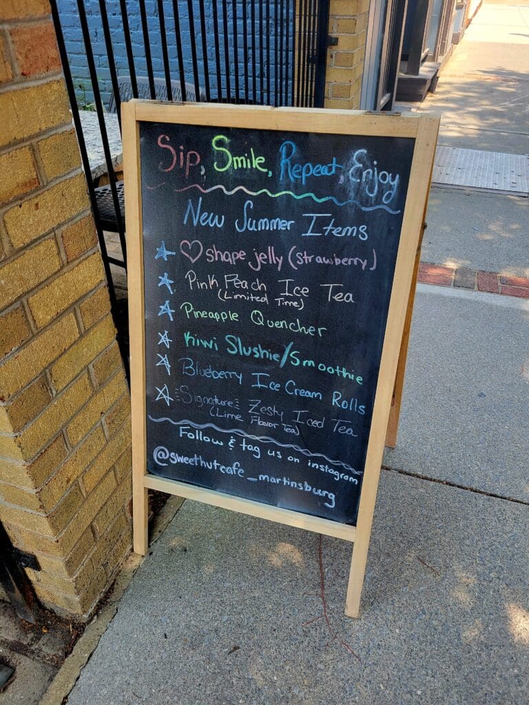 A wooden-framed chalkboard menu sign displays handwritten offerings on a city sidewalk outside a brick storefront.