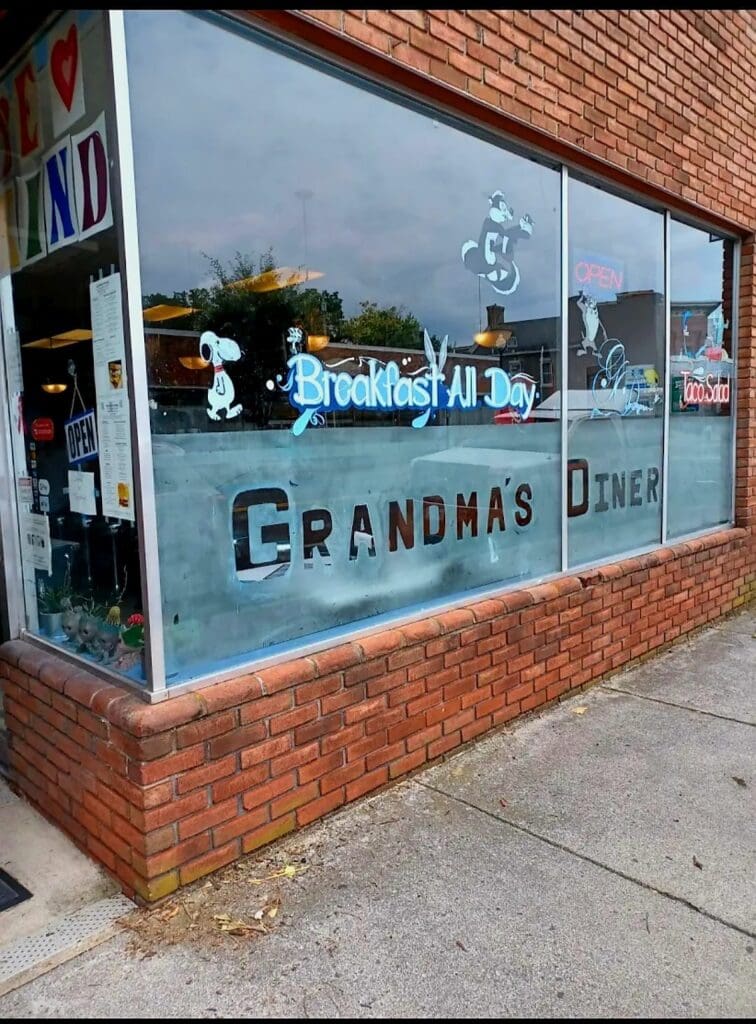 A vintage storefront window with blue-painted trim and 'Grandmas' signage on a red brick building facade, photographed during daytime.