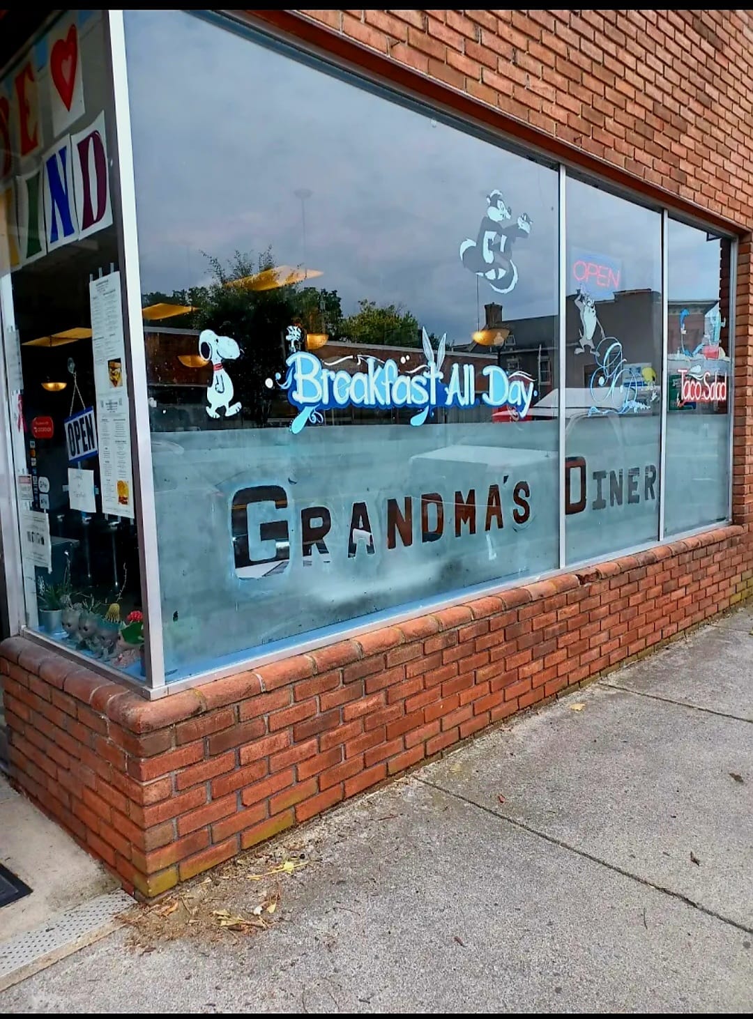 A vintage storefront window with blue-painted trim and 'Grandmas' signage on a red brick building facade, photographed during daytime.
