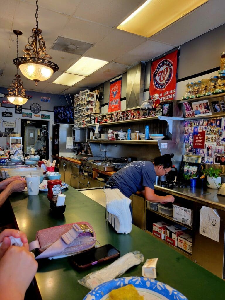 A cozy toy and collectibles shop interior with shelves displaying figurines, action figures, and merchandise, with staff members behind the counter.