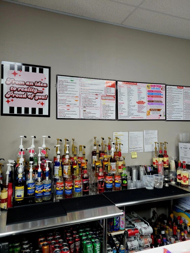 A well-organized display of various liquor and beverage bottles arranged on a black counter beneath informational wall charts in an indoor commercial or educational setting.