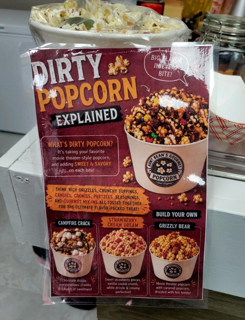 A product packaging box for 'Dirty Popcorn' displayed indoors, showing flavor variations and marketing text explaining the popcorn varieties.