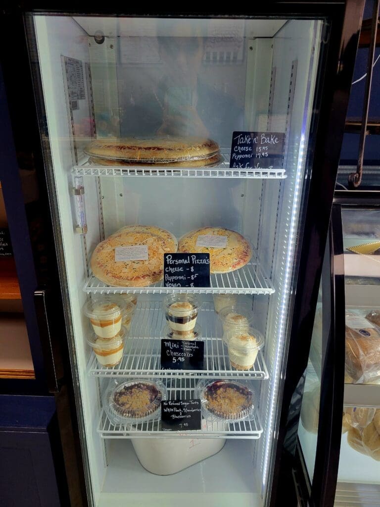 A glass-fronted refrigerated display case stocked with various baked goods and pastries including donuts and bread products.