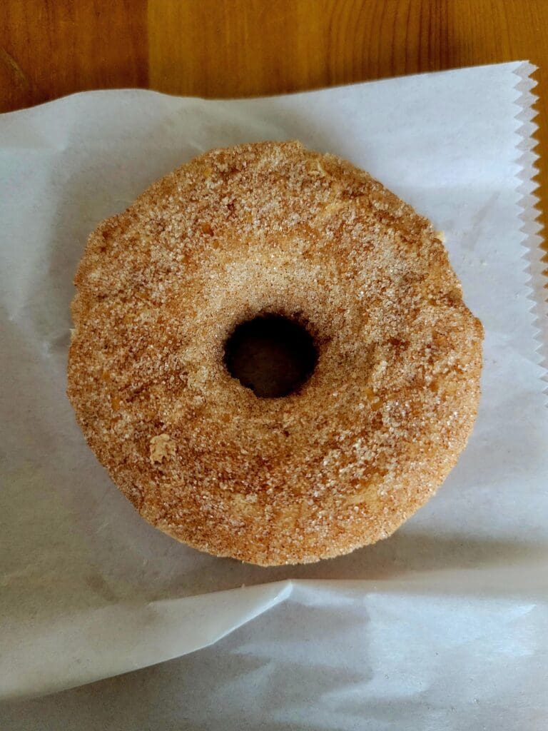 A golden cinnamon-sugar coated donut with a central hole sits on parchment paper against a wooden background.
