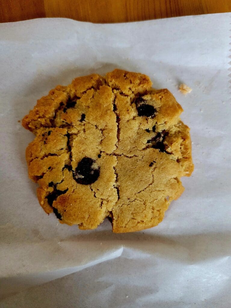 A freshly baked chocolate chip cookie rests on parchment paper, showing melted chocolate chips and a golden-brown exterior.