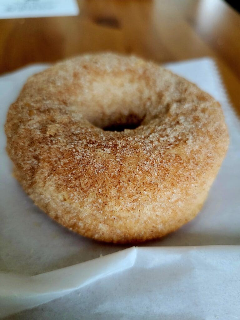 A close-up shot of a cinnamon sugar-coated donut with a hole in the center, placed on a white plate.