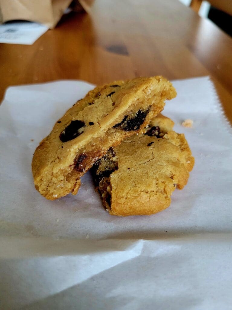 Three freshly baked chocolate chip cookies arranged on white parchment paper on a white plate.
