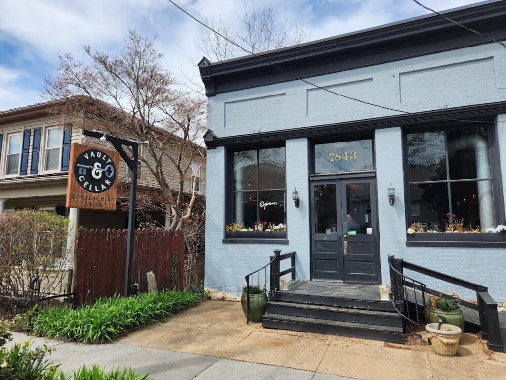 A charming contemporary storefront with modern dark-trimmed windows, a prominent wooden clock sign, and tasteful landscaping on a quiet day.