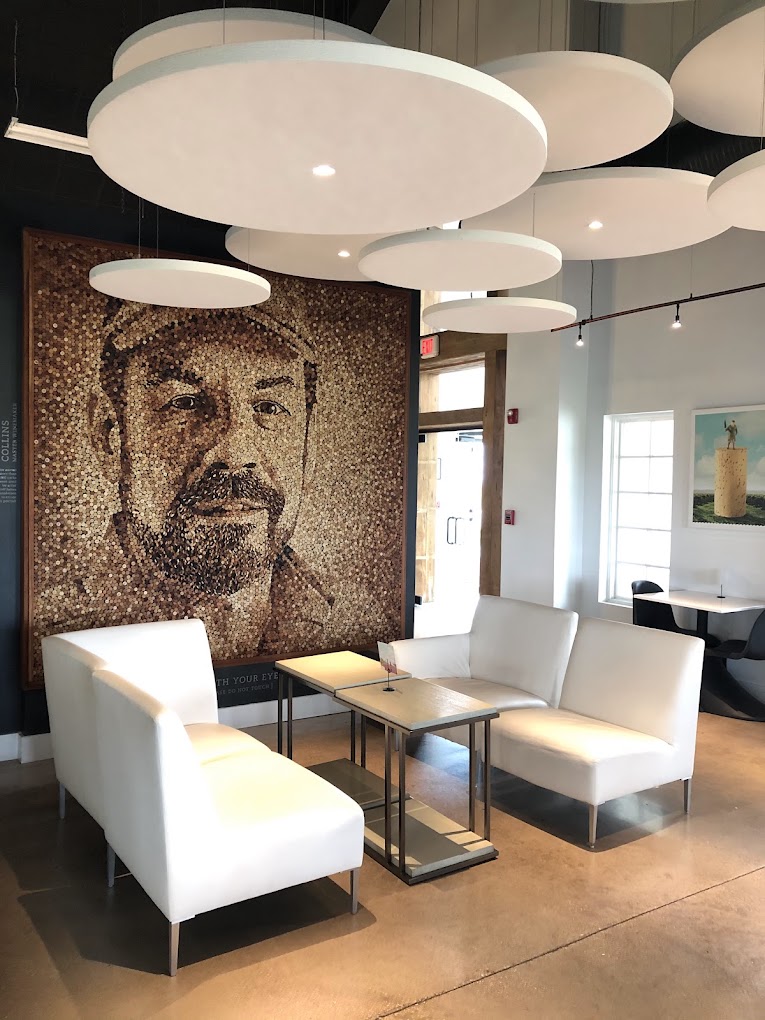 A contemporary office lounge features modern cloud-like ceiling lights, white seating, a minimalist wooden table, and a striking large-scale portrait artwork on the accent wall.