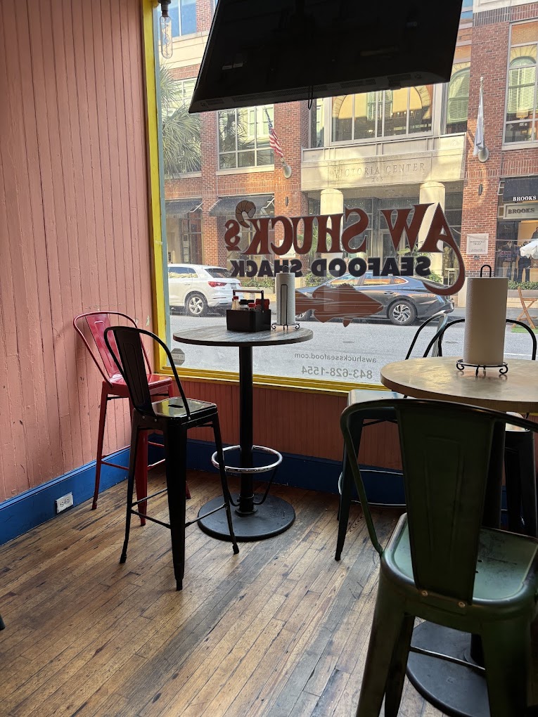 A cozy coffee shop interior with a round table and black chair near a window overlooking an urban street scene.