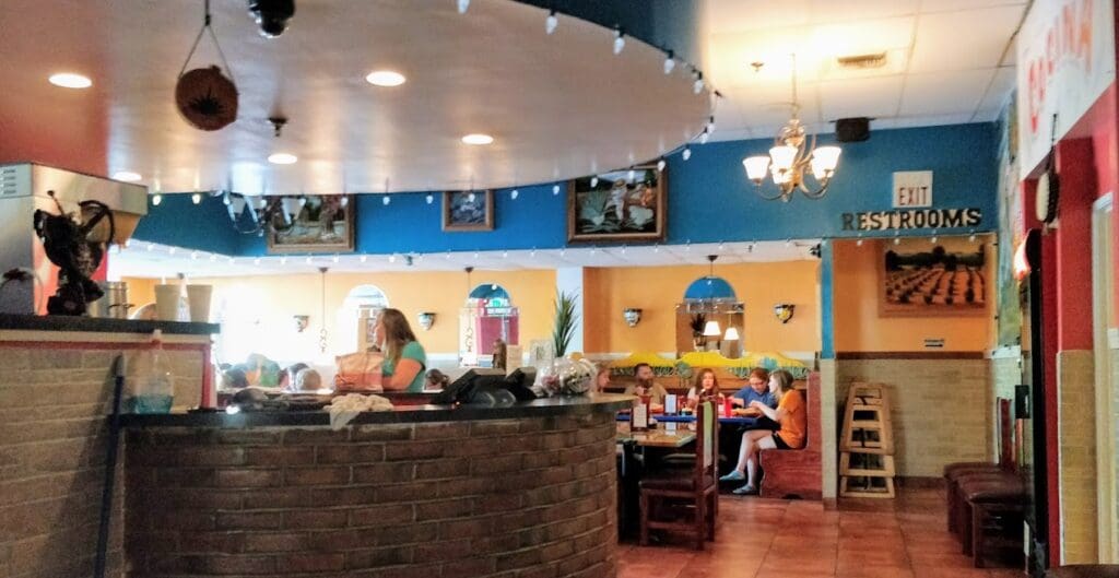 A bright, colorful ice cream shop interior with blue and yellow walls, a service counter with staff, and warm overhead lighting.