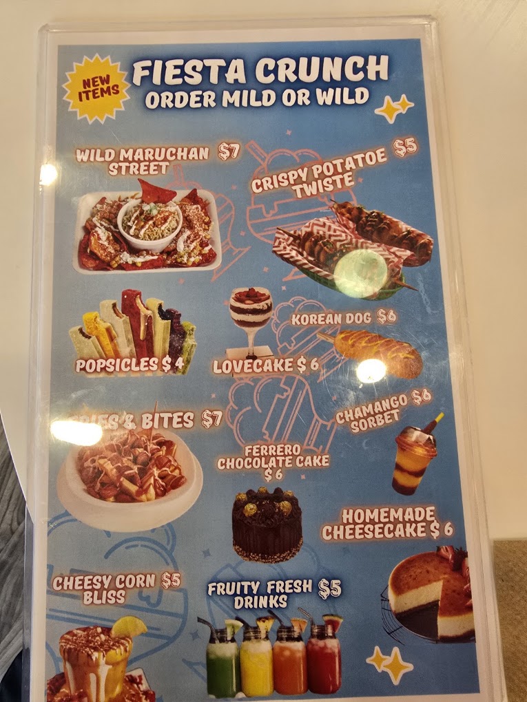 A Fiesta Crunch carnival food menu board displaying various fried and sweet treats with prices and colorful food photography.
