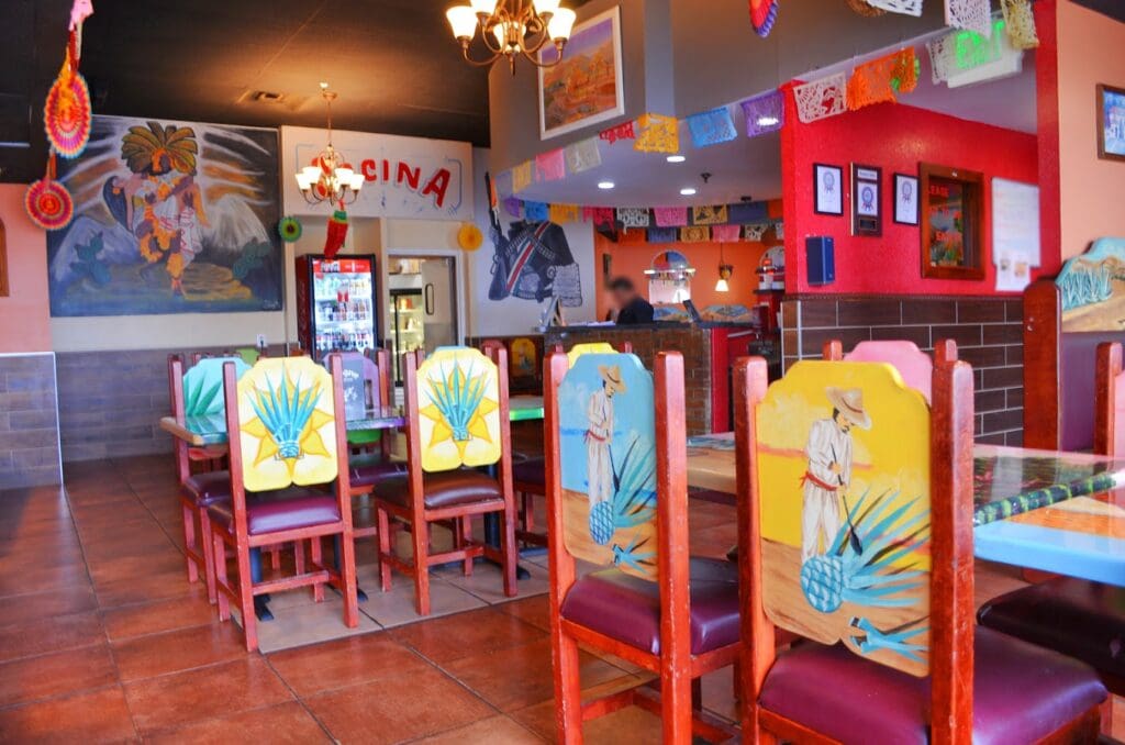 A colorful indoor children's play area and workshop space decorated with bright red structures, painted wooden chairs, and whimsical artwork panels.