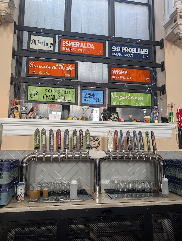 A modern bar setup with multiple beer taps and illuminated signage displaying various beverage options and drink names.